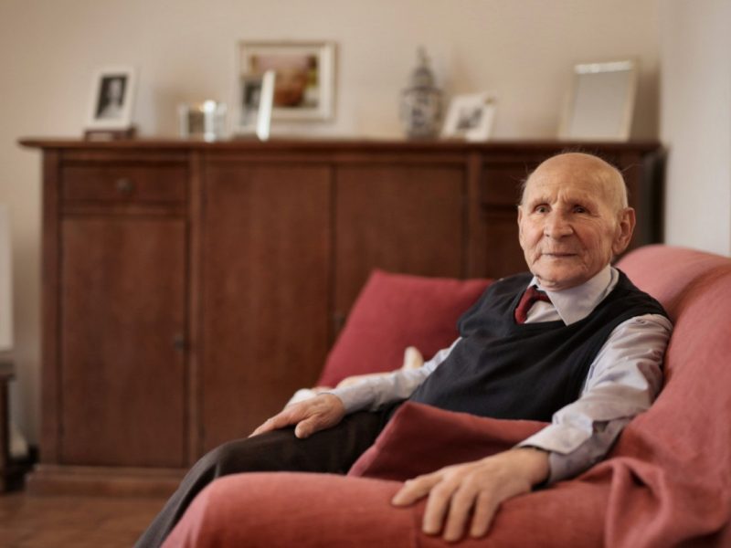 Alter Rentner sitzt auf rotem Sofa in seiner Wohnung